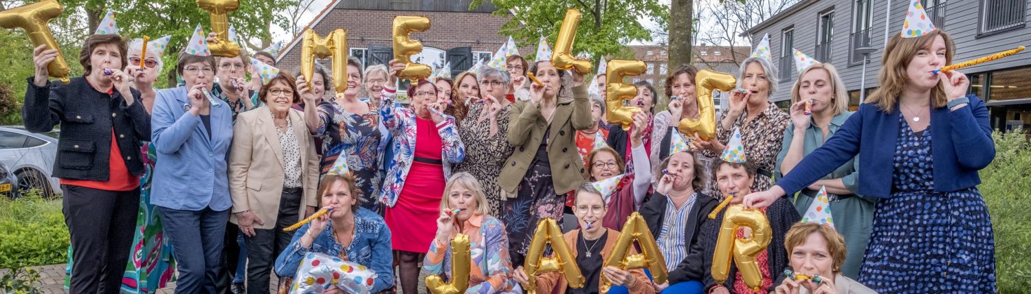 Groepsfoto van koor Timelez, allen met feesthoedjes op en de  tekst in ballonnen "timelez 5 jaar"